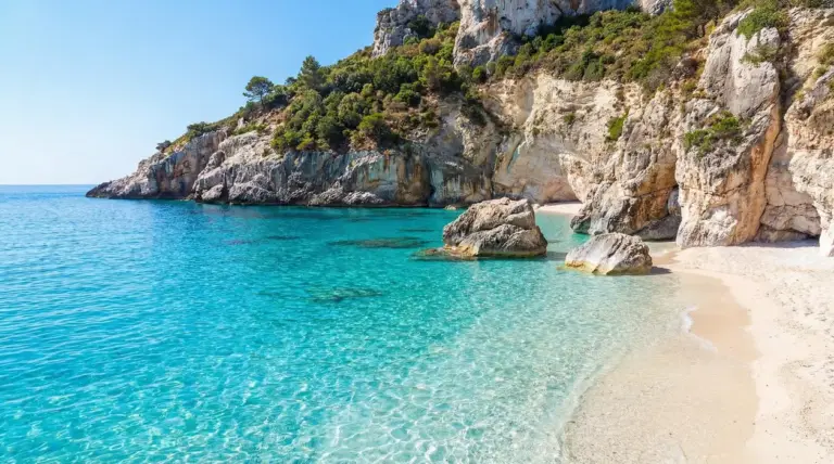 Spiaggia di sabbia chiara con mare turchese e scogliere rocciose, piccola baia tranquilla in Italia