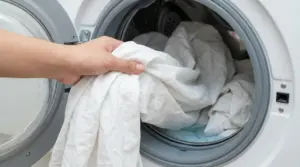 Mano che inserisce lenzuola bianche nella lavatrice a carica frontale per un lavaggio igienizzante