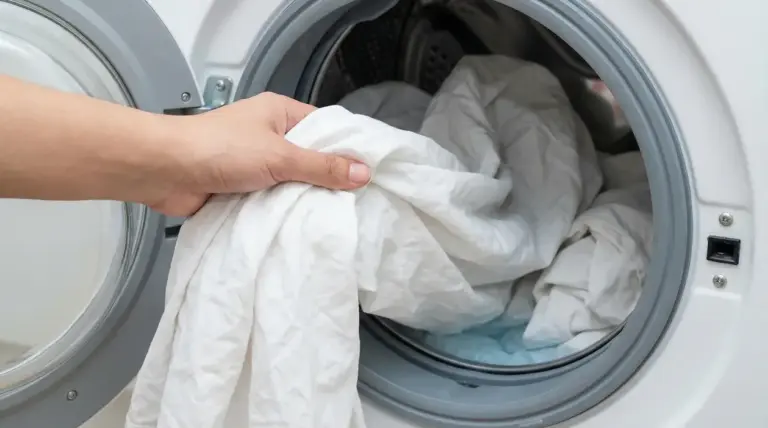 Mano che inserisce lenzuola bianche nella lavatrice a carica frontale per un lavaggio igienizzante