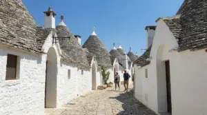 Vicolo tra i trulli di Alberobello con case bianche e tetti conici in pietra, visitatori che camminano